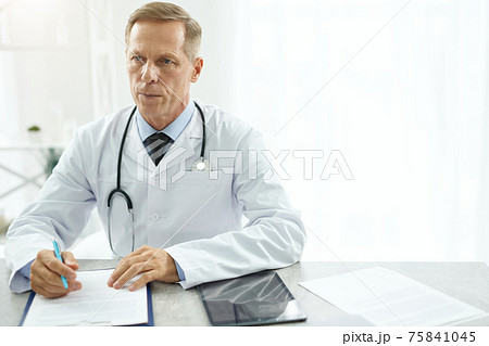 Serious male doctor sitting at the table in clinic Serious male doctor sitting at the table in clinic 75841045