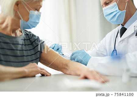 Doctor in sterile gloves injecting vaccine into patient arm 75841100