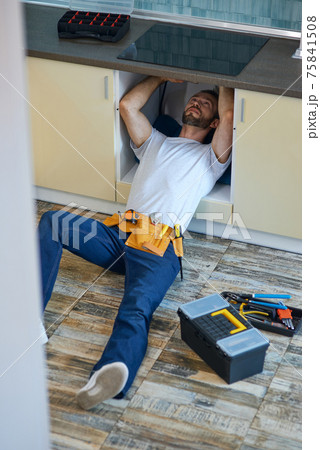 Stop leakage. Professional repairman, plumber wearing tool belt examining and fixing sink pipe in the kitchen indoors 75841508