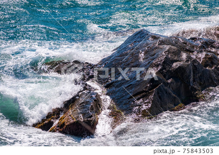 Sea waves of dark water beat against the coastal rocks. An infinite number of splashes, drops of water and white foam are scattered. 75843503