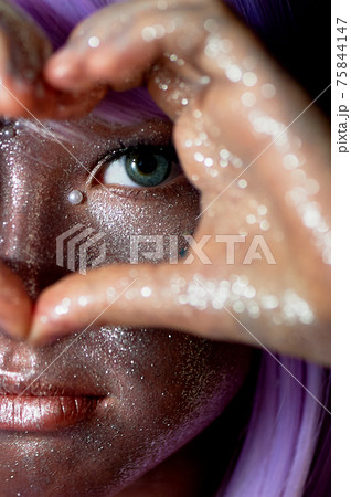 A girl with purple hair and glowing skin. An alien or a fairy with glowing skin. Her hands are folded in front of her face in a heart shape 75844147