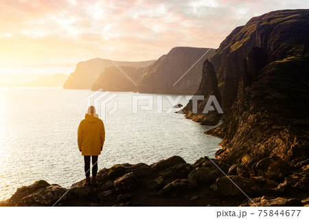 Tourist in yellow jacket looks at cliffs near Sorvagsvatn lake Tourist in yellow jacket looks at cliffs near Sorvagsvatn lake 75844677