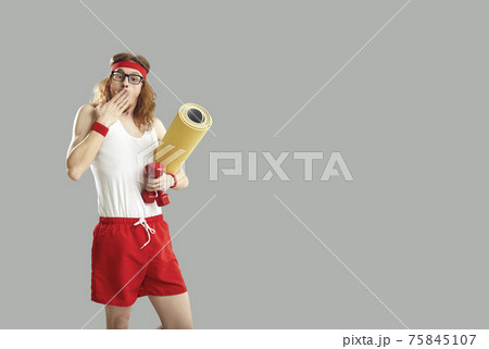 Surprised athlete in sportswear covers mouth with hand standing on gray background 75845107