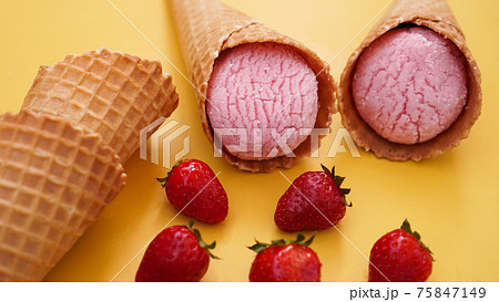 Strawberry ice cream in a waffle cone. Ice cream and berries on a yellow 75847149