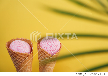 Two strawberry ice creams in a cone on a yellow background. Tropical leaf 75847161