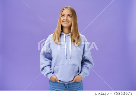 Winter comming. Dreamy kind and cute young girl with straight fair hair and tan wearing hoodie looking at upper left corner with nice white smile and admiring expression holding hand in pockets 75853675