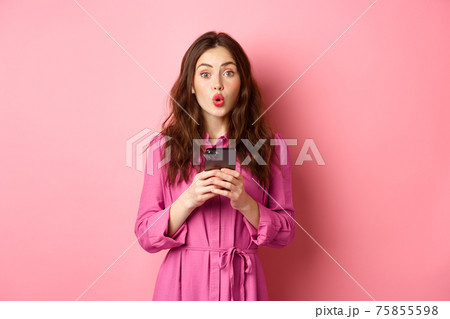Image of surprised young woman gasping and saying wow, staring impressed at camera after reading news online on mobile phone, standing with smartphone against pink background Image of surprised young woman gasping and saying wow, staring impressed at camera after reading news online on mobile phone, standing with smartphone against pink background 75855598