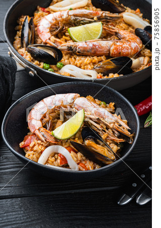 Typical spanish seafood paella in traditional pan and black bowl on black wooden background 75856905
