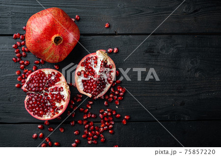 Ripe pomegranate with fresh juicy seeds, on black wooden table, top view with space for text 75857220