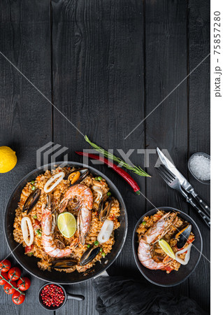 Typical spanish seafood paella in traditional pan and black bowl on black wooden background, flat lay with copy space Typical spanish seafood paella in traditional pan and black bowl on black wooden background, flat lay with copy space 75857280