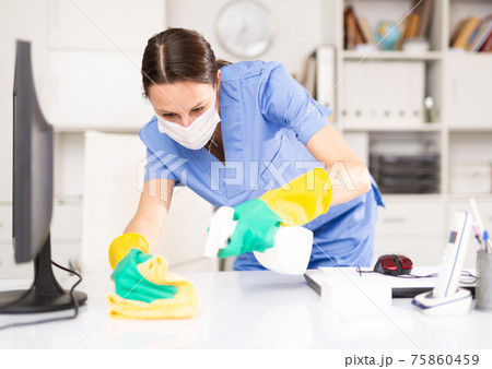 Woman in protective mask wipes dust from table in office 75860459