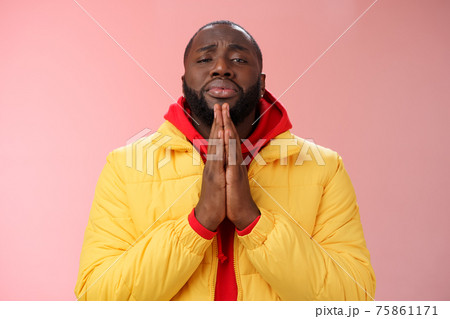 Miserable cute african-american bearded man in yellow coat asking help begging press palms supplicating apologizing please help, standing pink background sad need advice lending money 75861171