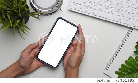 Mock up image of young woman holding smart phone with blank screen on white desk. Mock up image of young woman holding smart phone with blank screen on white desk. 75861395