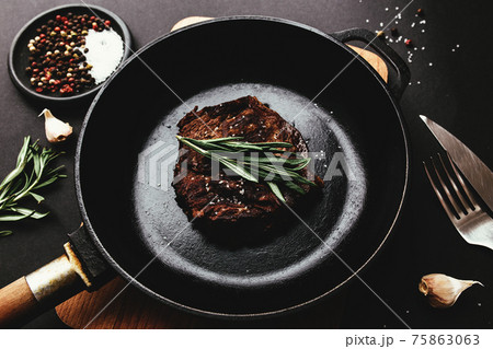 Ribeye steak on cast-iron pan, board with rosemary, garlic, knife, fork, salt 75863063