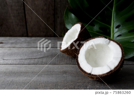 Broken coconuts on gray wooden background with palm leaf. White coconut pulp 75863260