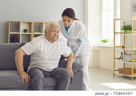Friendly female doctor helps an older man who is trying to get up from the couch. 75864367