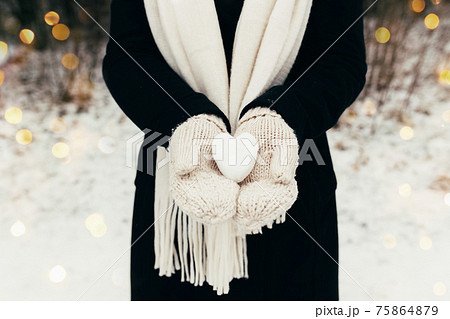 Snow heart snowball in girl gloved hands. Blurred background 75864879