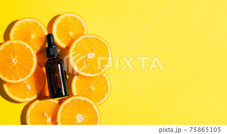 A bottle of cosmetic product oil serum gel made from a juicy ripe orange on a bright yellow background 75865105