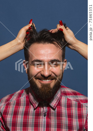Female hands rumple young bearded handsome man on blue background Female hands rumple young bearded handsome man on blue background 75865351