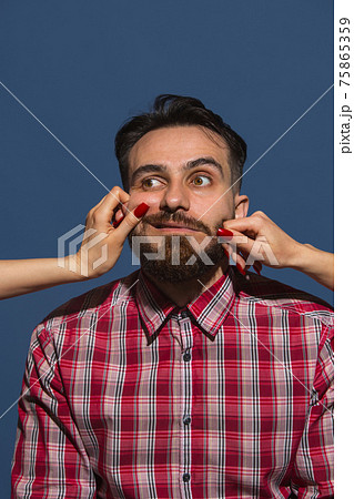 Female hands making different emotions of young bearded man on blue background Female hands making different emotions of young bearded man on blue background 75865359