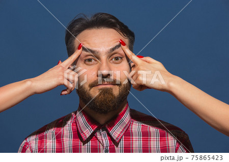 Female hands opening eyes of young bearded handsome man on blue background Female hands opening eyes of young bearded handsome man on blue background 75865423
