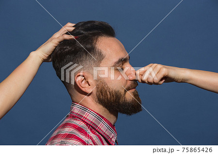 Female hands making different emotions of young bearded man on blue background Female hands making different emotions of young bearded man on blue background 75865426