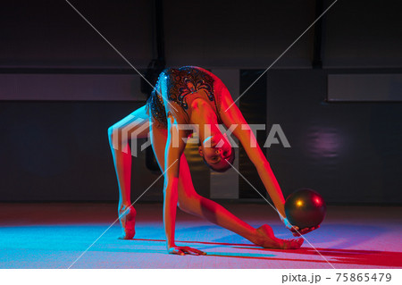 Young graceful girl rhythmic gymnast isolated on dark background in neon light Young graceful girl rhythmic gymnast isolated on dark background in neon light 75865479