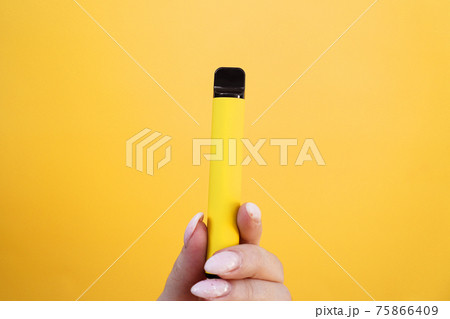 Yellow disposable electronic cigarette in female hand. Bright yellow background Yellow disposable electronic cigarette in female hand. Bright yellow background 75866409