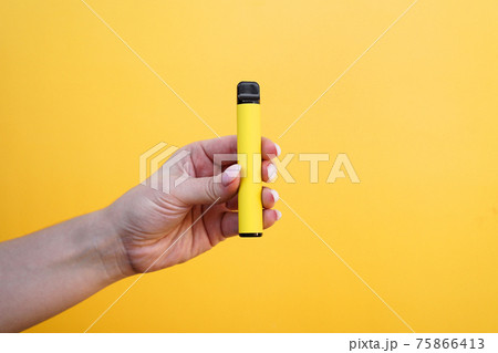 Yellow disposable electronic cigarette in female hand. Bright yellow background Yellow disposable electronic cigarette in female hand. Bright yellow background 75866413