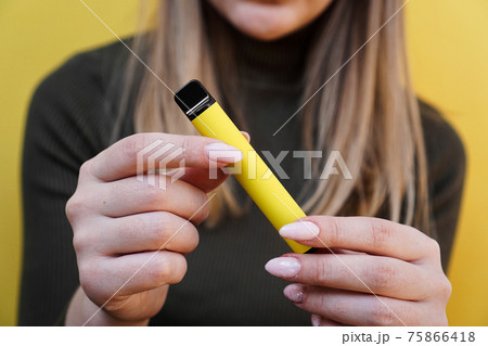 Yellow disposable electronic cigarette in female hand. Bright yellow background Yellow disposable electronic cigarette in female hand. Bright yellow background 75866418