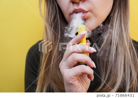 A young girl smokes disposable electronic cigarette. Bright yellow background A young girl smokes disposable electronic cigarette. Bright yellow background 75866431