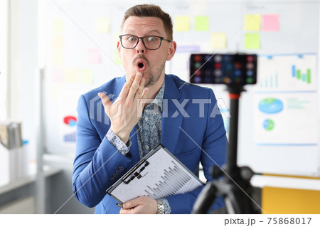 Surprised business coach with documents in hands looking at camera of mobile phone 75868017