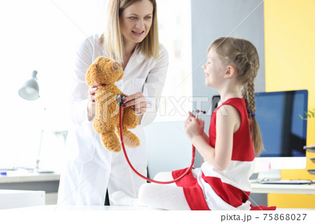 Little girl listening to toy bear with stethoscope together with doctor 75868027