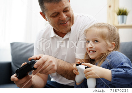 Grandfather and granddaughter playing video games at home. Grandfather and granddaughter playing video games at home. 75870232