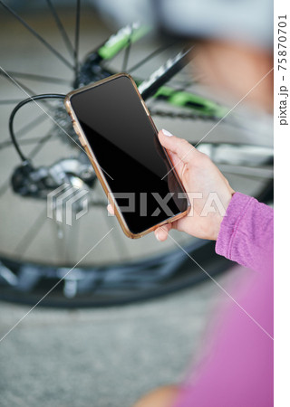 Close up shot of hand of female cyclist holding smartphone while checking her bicycle mechanisms, sprocket and chain on a mountain bike outdoors on a daytime 75870701