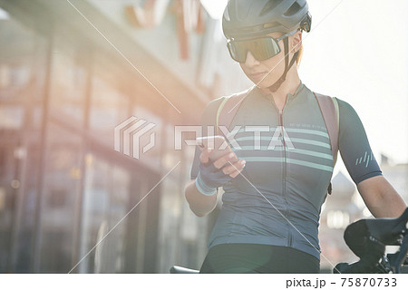 Female cyclist in protective gear using smartphone while riding bicycle in city center. Sportswoman training, exercising outdoors 75870733