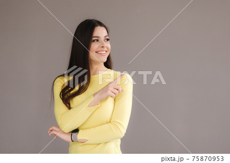 Portrait of attractive woman in yellow sweatshirt point the finger at place for text. Female on grey background Portrait of attractive woman in yellow sweatshirt point the finger at place for text. Female on grey background 75870953