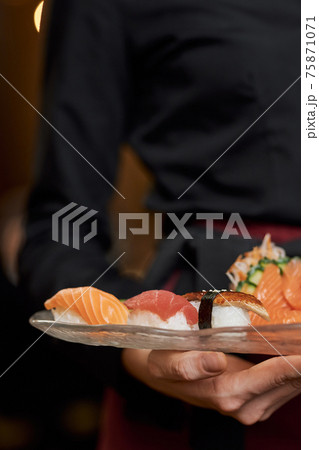Appetizing sushi on plate in hands of restaurant staff Appetizing sushi on plate in hands of restaurant staff 75871071