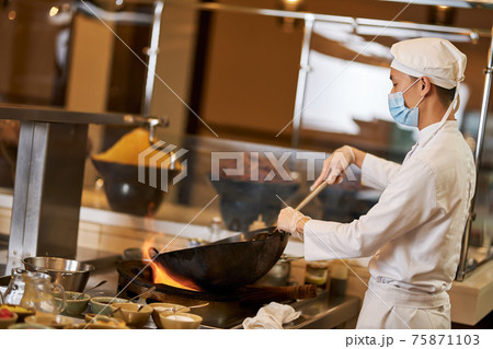 Focused kitchen staff wearing mask and cooking in the wok 75871103