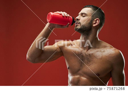 Adult Caucasian bearded athlete holding red bottle with beverage on red background 75871268