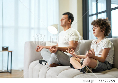 Peaceful vibes. Relaxed latin middle aged father and his son meditating together on a couch at home 75872259