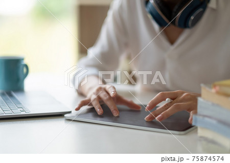Close up of female worker working from home with digital tablet, laptop and headphone in home office room. 75874574