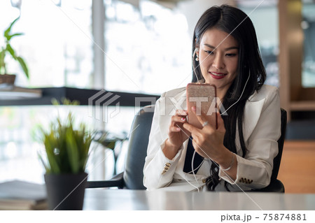 Relax Time - Businesswoman with headphones using smartphone for listening music sitting at the desk indoors in office. 75874881