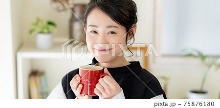 リビングで赤いマグカップでカフェオレを飲む若い女性の顔のアップ　バナーサイズ 75876180