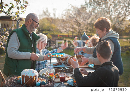 The family gathered at a festive table in the garden to celebrate Easter The family gathered at a festive table in the garden to celebrate Easter 75876930