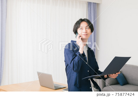 リビングのテーブルに腰かけて資料を確認する若い男性 リビングのテーブルに腰かけて資料を確認する若い男性 75877424