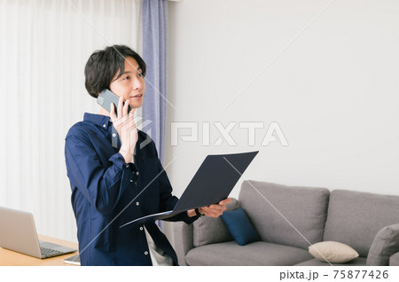 リビングのテーブルに腰かけて資料を確認する若い男性 リビングのテーブルに腰かけて資料を確認する若い男性 75877426