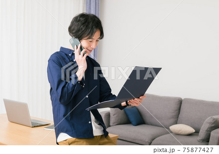 リビングのテーブルに腰かけて資料を確認する若い男性 リビングのテーブルに腰かけて資料を確認する若い男性 75877427