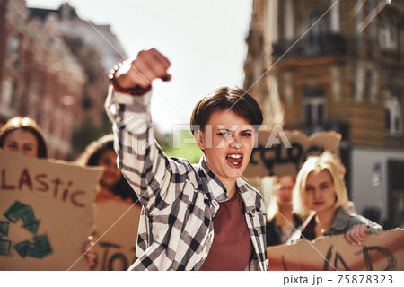 Emotional young woman screaming a slogan and leading a group of demonstrators on the road 75878323