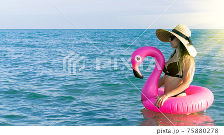 Summer hat beach. Happy young sexy girl in bikini swimsuit, sunglasses and straw hat with pink inflatable flamingo in blue sea water on ocean background. Luxury lifestyle travel. 75880278